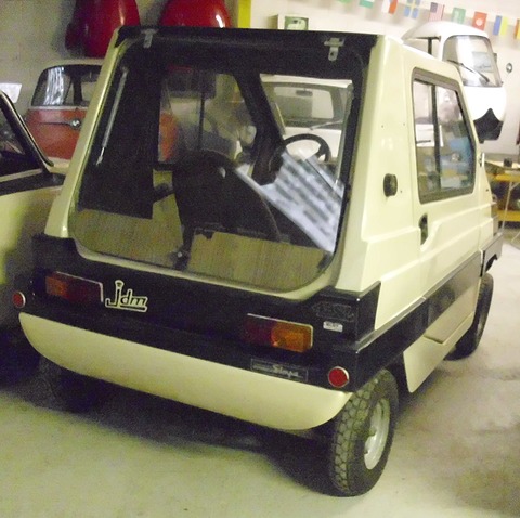 Back of a small cream and black boxy car with a large glass tailgate, orange rear lamps and chunky tyres.
