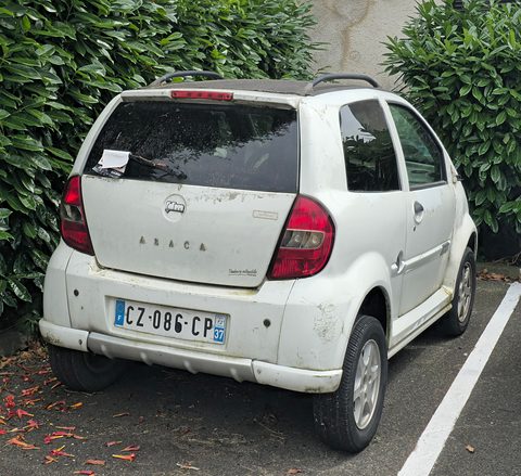 Rear of a grubby white small hatchback with ABACA lettering and plate CZ-086-CP, parked in a bay before a laurel hedge. Opens a larger view