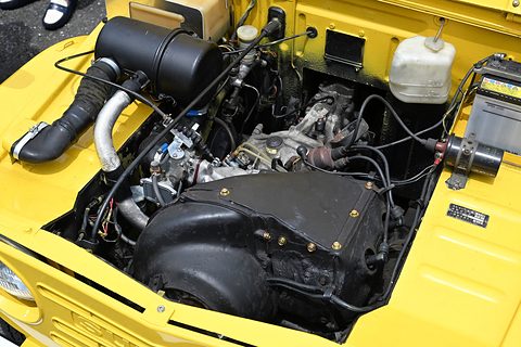 Open yellow bonnet over a black engine with a large air-cooling duct, a ribbed silver hose and a white reservoir.