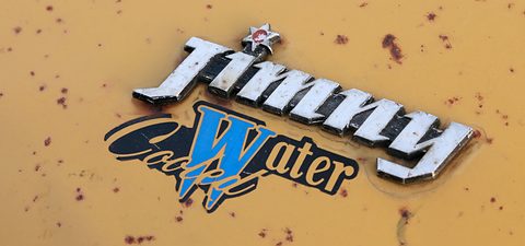 Chrome Jimny script with a small star over a blue and black Water Cool emblem, on mustard paint with rust spots. Opens a larger view