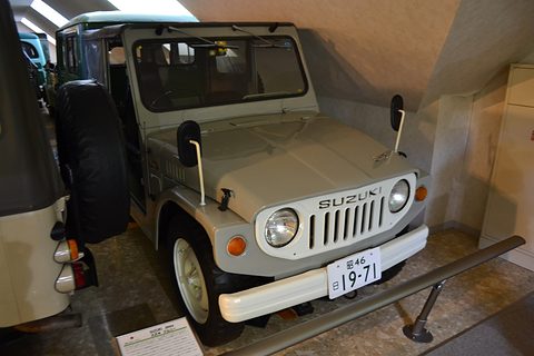 White small 4x4 with a soft top, round headlamps, a slotted grille and a Japanese plate, behind a low rail in a museum. Opens a larger view