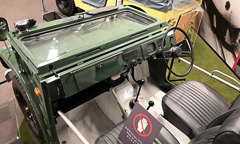 Green small 4x4 from above: flat painted dashboard with central dials, a thin steering wheel, black pleated seats and a gear lever. Opens a larger view