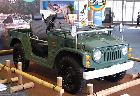 Green open small 4x4 with black bucket seats, round headlamps and a white bumper, on a stand fenced with bamboo poles. Opens a larger view