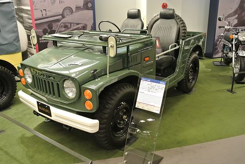 Green open small 4x4 with a roll bar, grey seats and a white bumper on a green museum floor, an information placard beside it. Opens a larger view