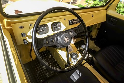 Yellow painted dashboard with round dials, a black steering wheel with a Suzuki horn button and a black ribbed seat. Opens a larger view