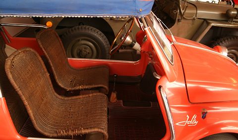 Close view into an open orange Fiat 500 body with two woven wicker seats, a wicker floor mat and a slim steering wheel.