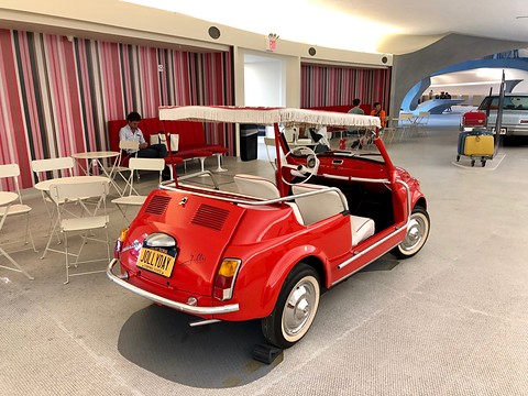 Rear three-quarter view of a red doorless beach car with a fringed canopy, white seats and a louvred engine lid. Opens a larger view