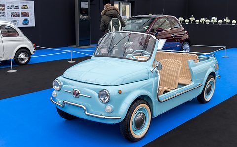 Pale blue doorless open car with a long wicker rear bench and whitewall tyres, on a blue and black carpeted stand.