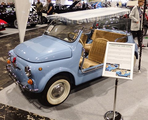 Pale blue doorless Fiat 500 with cane seats and a striped awning, an information board on a stand in front. Opens a larger view