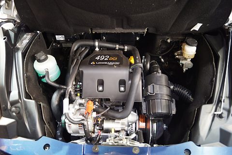 Compact engine bay with a black engine cover marked 492 DCI Lombardini, hoses, an air filter and a coolant bottle. Opens a larger view