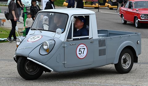 Grey three-wheeled pickup with a white cab and a red-ringed number 57 on the door, people standing behind. Opens a larger view