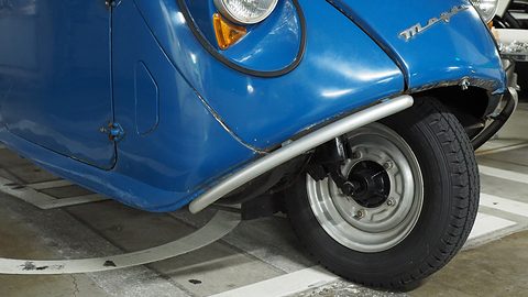 Close view of a blue rounded nose with a chrome bumper strip curving over a single front wheel. Opens a larger view