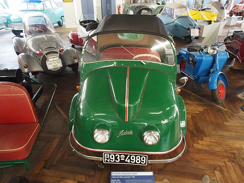 Green three-wheeler facing the camera with plate BN 93-4989, a grey microcar and blue scooter beside it. Opens a larger view