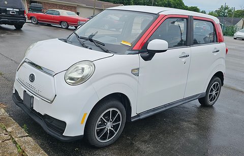 White small four-door car with a red roof pillar and round headlamps on a wet car park. Opens a larger view