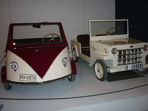 A maroon and cream open microcar with a V-shaped two-tone nose beside a white jeep-style microcar with a bar grille. Opens a larger view