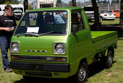 Bright green cab-over pickup on grass, a man standing at its left. Opens a larger view