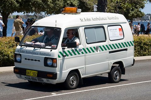 White van with green chevrons and St John Ambulance lettering on a road, two crew in the cab. Opens a larger view