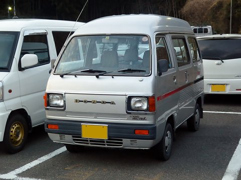Silver high-roof cab-over van with a red stripe in a car park beside white vans. Opens a larger view