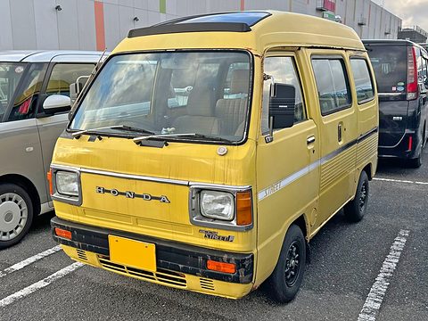 Yellow high-roof cab-over van in a car park, a silver car beside it. Opens a larger view