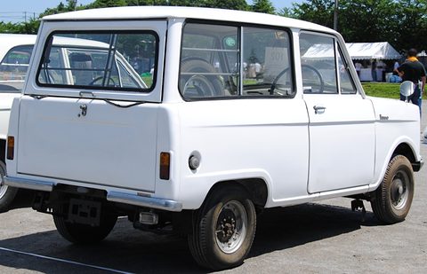 Rear three-quarter of a white small van with a split tailgate, cars and a marquee behind. Opens a larger view