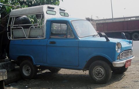 Blue small pickup with a white cover over its bed, parked on dusty ground. Opens a larger view
