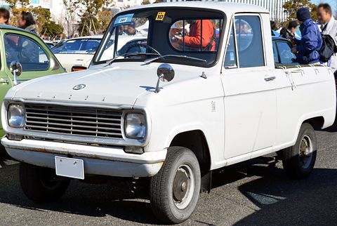 White small pickup with a bonnet and round headlamps among visitors and cars. Opens a larger view