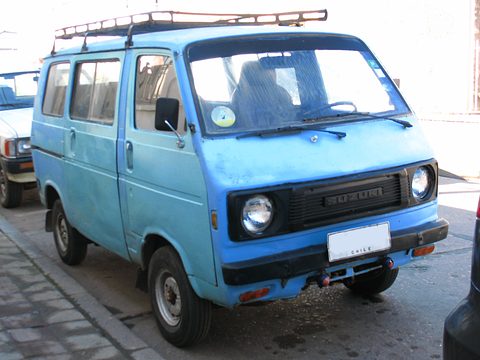 Pale blue cab-over van with a roof rack parked by a kerb. Opens a larger view