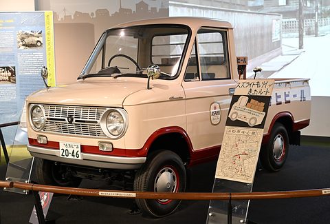 Cream and red small pickup with lettered doors behind a rope barrier and a display sign. Opens a larger view