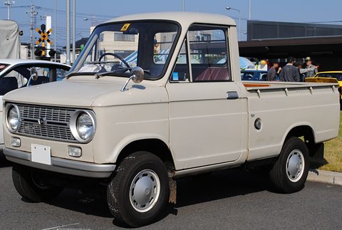 Cream small pickup with a short bonnet and round headlamps, a level crossing behind. Opens a larger view