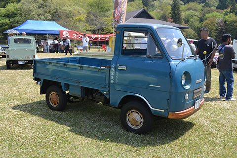 Blue cab-over pickup on grass, visitors and marquees behind. Opens a larger view