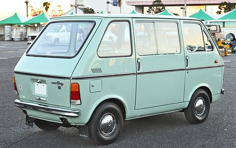 Rear three-quarter of a mint-green van with large windows, marquees behind. Opens a larger view