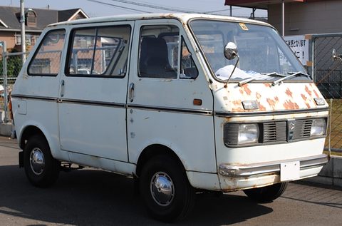 White cab-over van with rust patches on its nose, parked by a fence. Opens a larger view