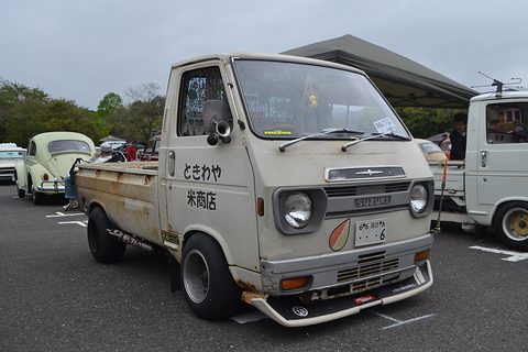 Grey cab-over pickup with Japanese shop lettering on its door and aftermarket wheels. Opens a larger view