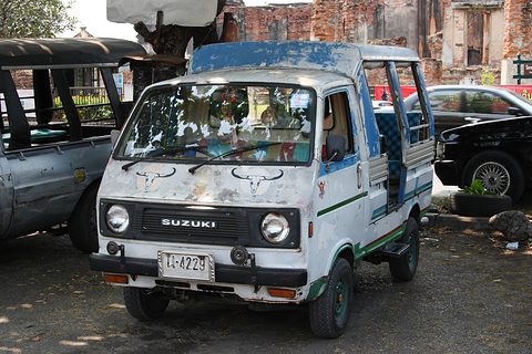 Battered white cab-over pickup with a roofed passenger bed and painted horns on its nose. Opens a larger view