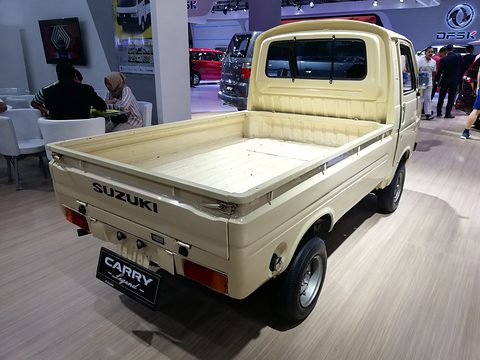 Cream cab-over pickup seen from behind on a wooden floor, a CARRY plate on its tailboard. Opens a larger view