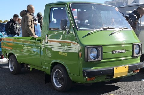 Green cab-over pickup with a stripe, men in winter coats standing behind it. Opens a larger view