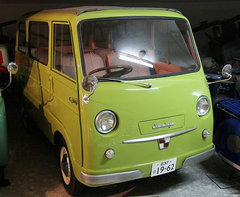 Lime-green small cab-over van with round headlamps and a chrome bar on its nose, in a museum.