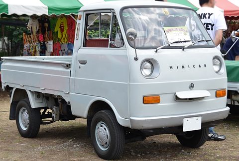 Grey cab-over pickup with MINICAB letters on its nose under a green-and-white awning. Opens a larger view
