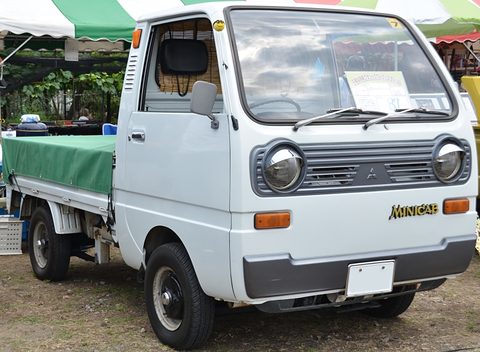 White cab-over pickup with a dark grille and a green cover over its bed. Opens a larger view