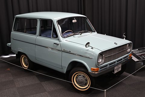 Pale blue small estate van with whitewall tyres in front of black drapes. Opens a larger view