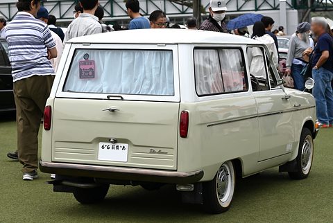 Rear view of a pale green estate van with curtains, visitors around it on artificial grass. Opens a larger view