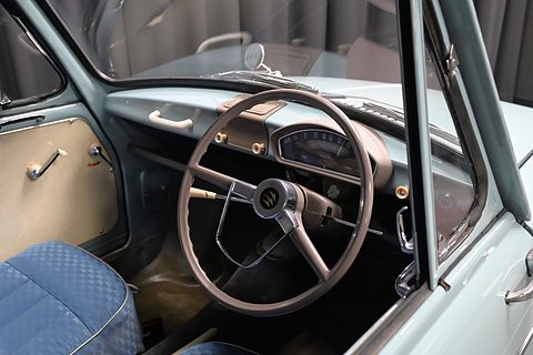 Through an open door: a thin two-spoke steering wheel, a pale blue dashboard and a blue seat. Opens a larger view