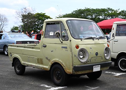 Pale green cab-over pickup with round headlamps and worn paint, on a car park. Opens a larger view