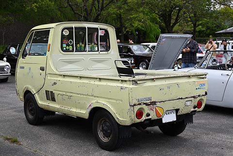 Rear three-quarter of a pale green cab-over pickup with stickers on its back window. Opens a larger view