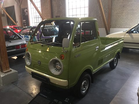 Olive-green cab-over pickup in a brick hall with wooden beams. Opens a larger view