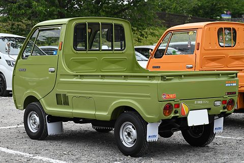 Rear three-quarter of a bright olive cab-over pickup with mud flaps, on gravel. Opens a larger view