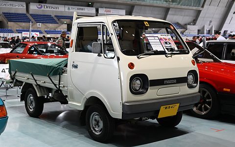 White cab-over pickup with a green cover over its bed, on a show floor. Opens a larger view