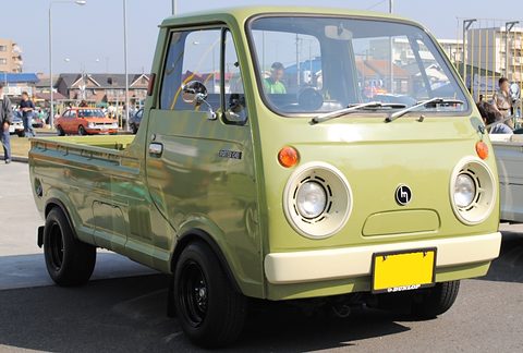 Olive-green cab-over pickup with round headlamps and a yellow plate.
