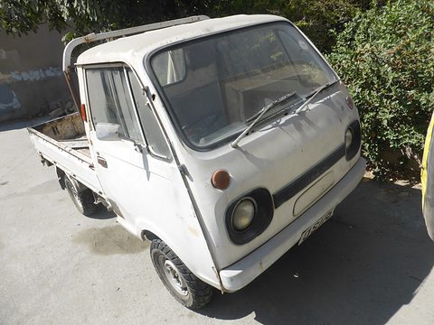 Dusty white cab-over pickup parked under a bush on a sloping street. Opens a larger view