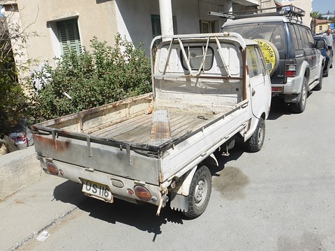 Rear three-quarter of a worn white cab-over pickup with a rack behind its cab. Opens a larger view